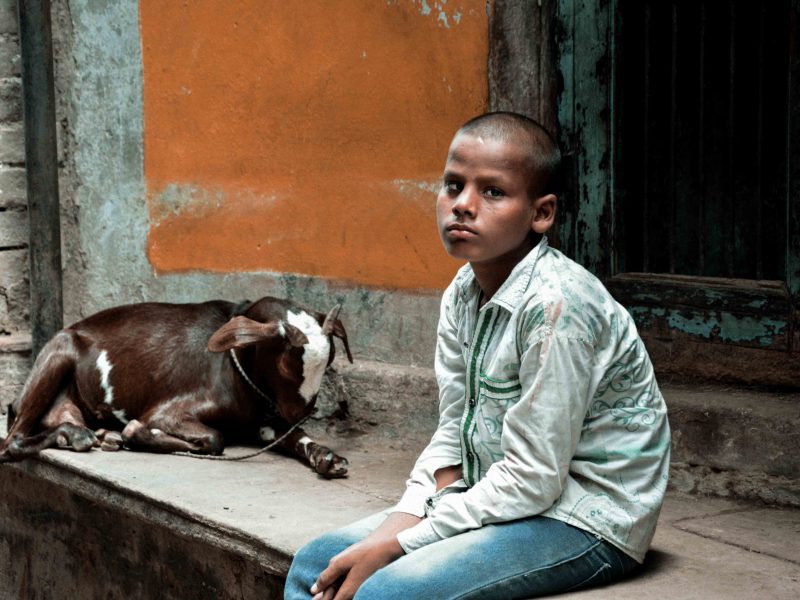 Bambino nelle strade di Varanasi con la sua capretta, India
